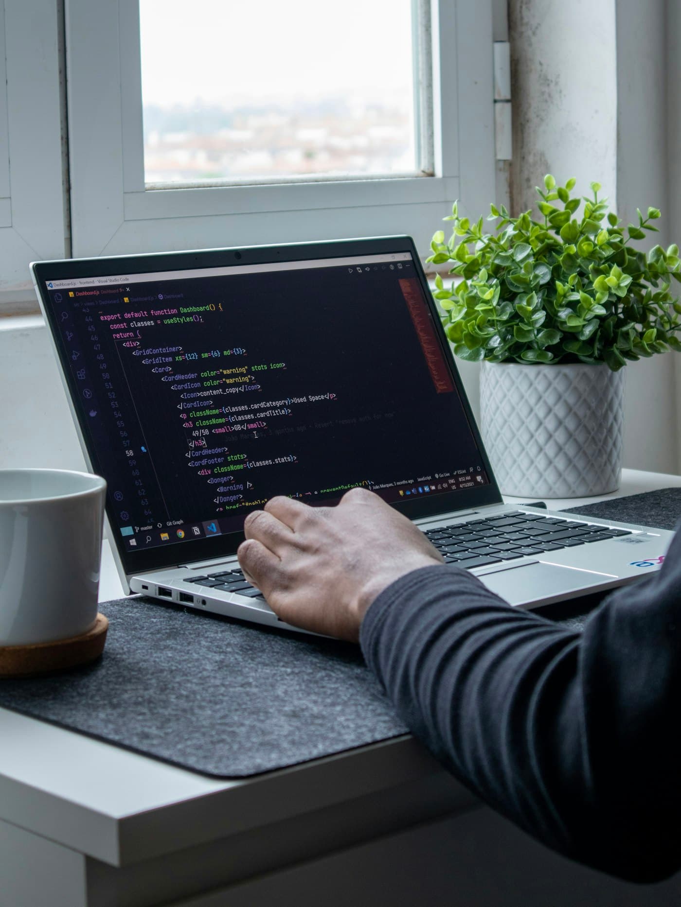 Hands typing code on a laptop beside a plant